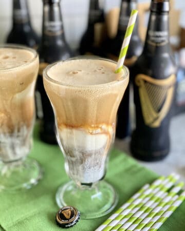 Close up of a glass filled with ice cream and Guinness beer with another glass and beer bottles in background.