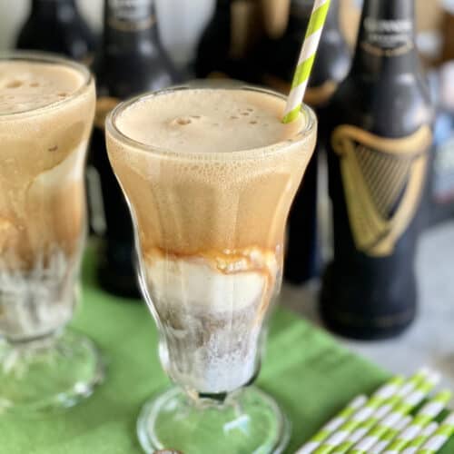 Close up of a glass filled with ice cream and Guinness beer with another glass and beer bottles in background.