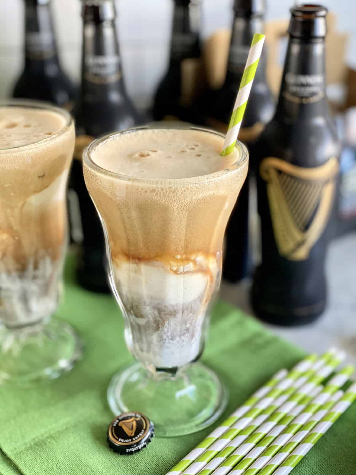 Close up of a glass filled with ice cream and Guinness beer with another glass and beer bottles in background.