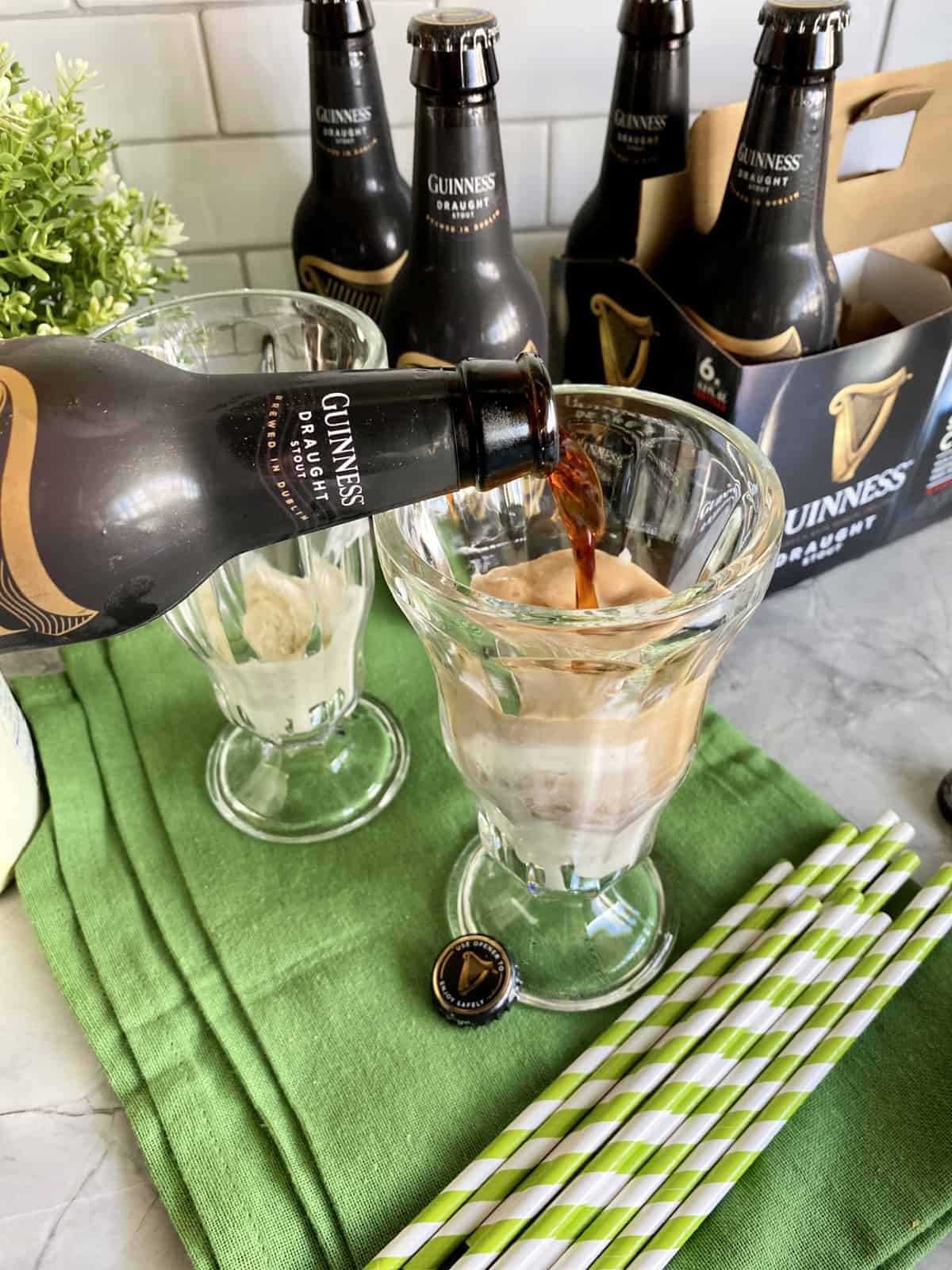 Guinness being poured into a tall glass with beer bottles in background.