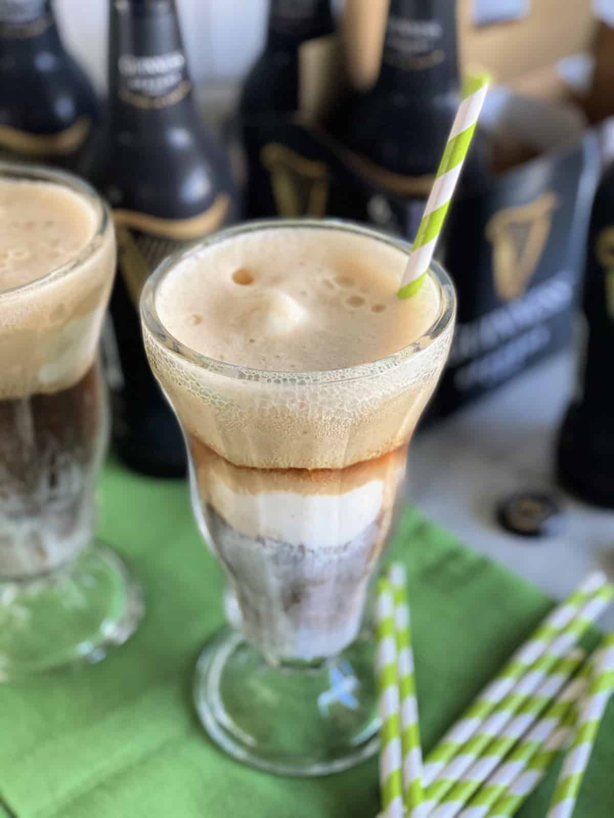 Glass filled with beer and ice cream with a green and white paper straw.