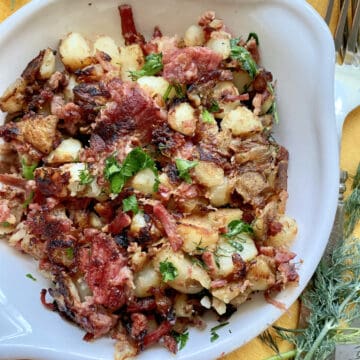 Top view of a white dish filled with fried Corned Beef Hash and herbs.
