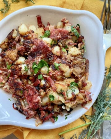 Top view of a white dish filled with fried Corned Beef Hash and herbs.