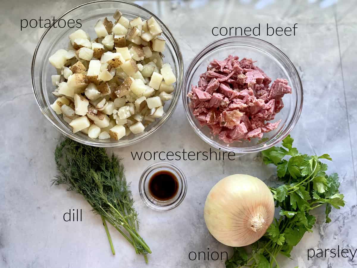Ingredients on marble countertop: potatoes, corned beef, dill, worcestershire, onion, and parsley.