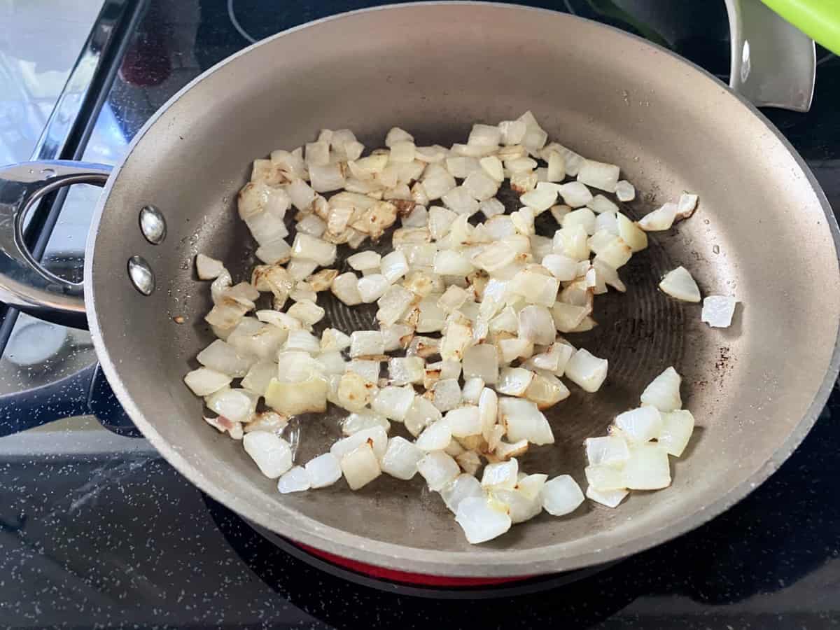 Brown skillet filled with slightly browned diced onions.