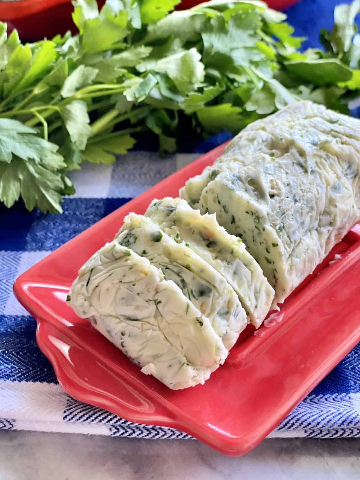 Red butter dish with a log of Garlic Herb Butter with three slices cut from it.