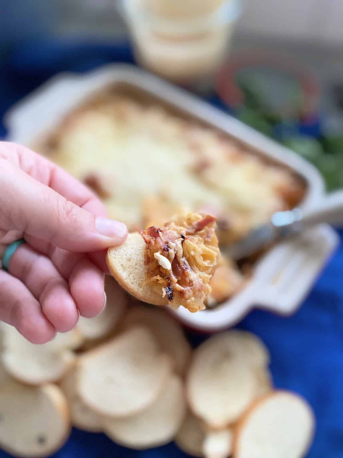 Female hand holding a bagle chip filled with Hot Reuben Dip.