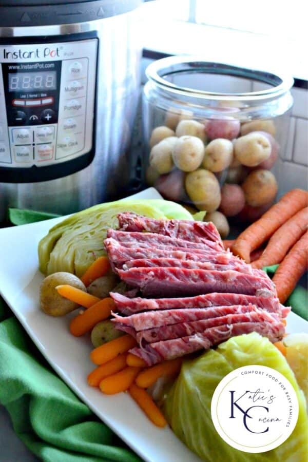 White platter filled with potatoes, baby carrots, quartered cabbage and corned beef with a logo on the right corner.