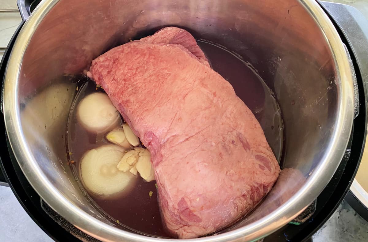 Top view of raw corned beef and onions in an Instant Pot.