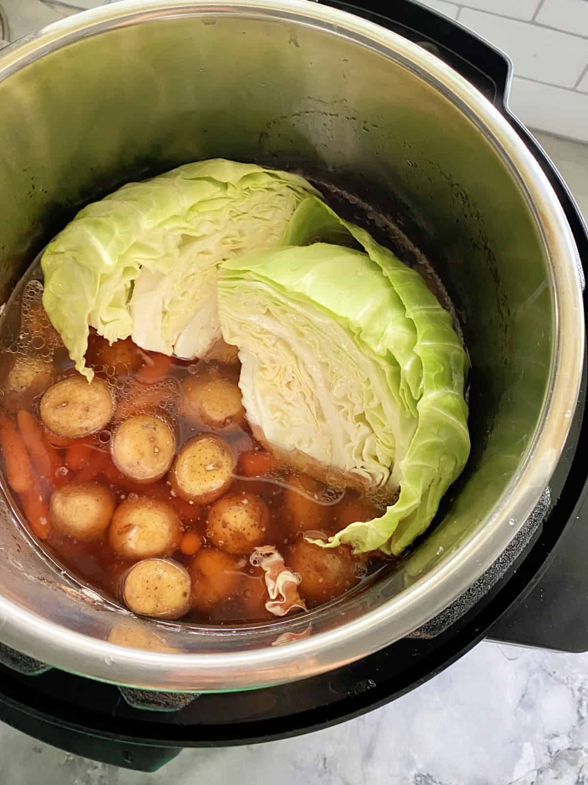 Top view of a quartered cabbage and cooked potatoes and baby carrots in an Instant Pot.