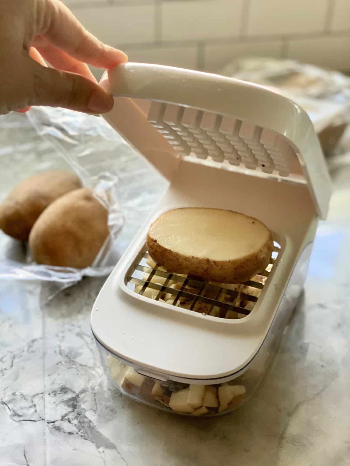 Female hand holding up a lid to a vegetable dicer with a potato on the sharp plate.