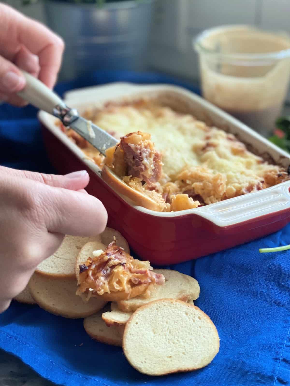 Female hand scooping dip onto a toasted baguette using a knife.