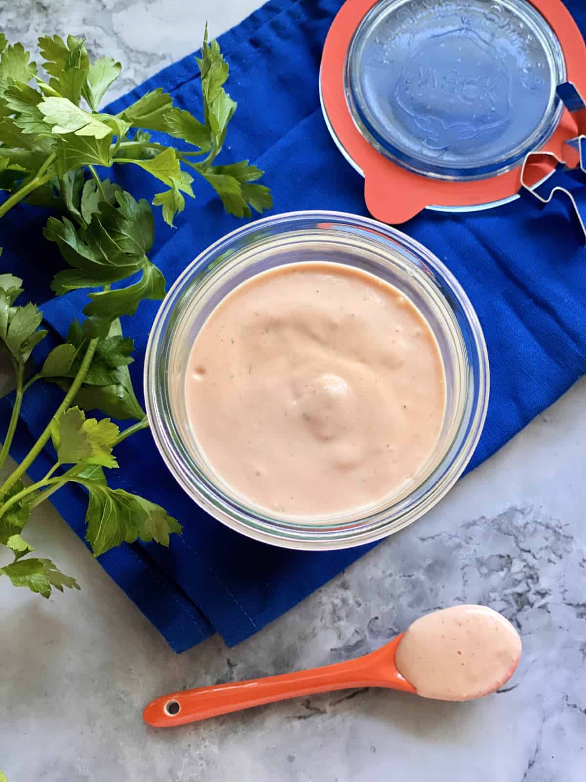 Top view of a glass jar of sauce with a spoon filled with the sauce and parsley next to it.