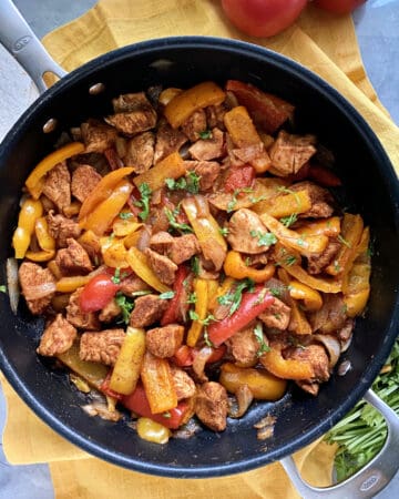 Top view of a large skillet filled with chicken and multi-colored peppers.