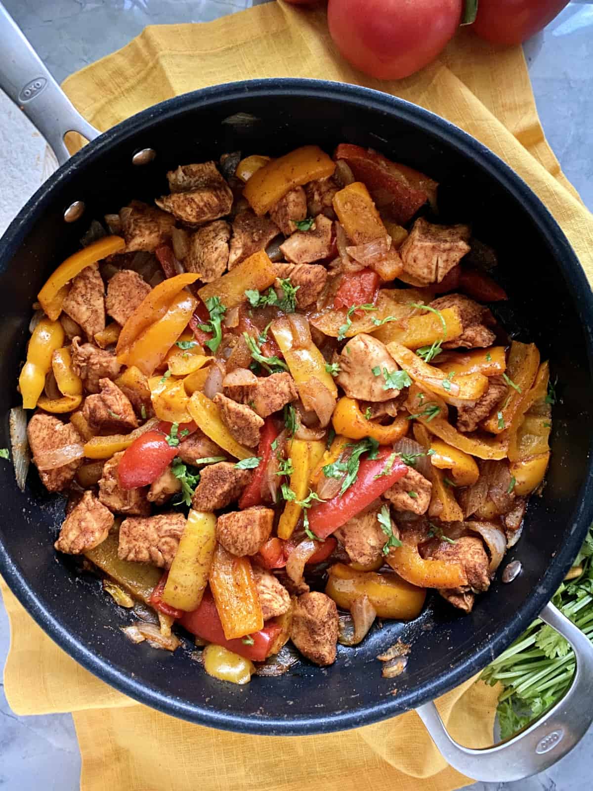 Top view of a large skillet filled with chicken and multi-colored peppers.