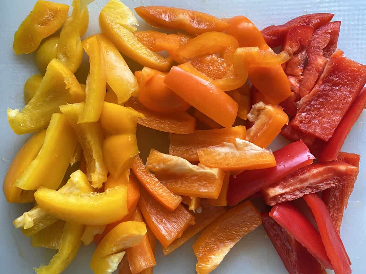 Yellow, Orange, and Red Bell peppers sliced on a cutting board.