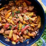 Top view of a skillet with chicken, bell peppers, and onions with cilantro sprinkled on top.