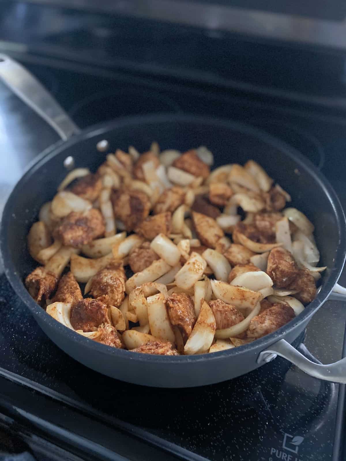 Skillet cooking on a glasstop stove filled with chicken and onions.