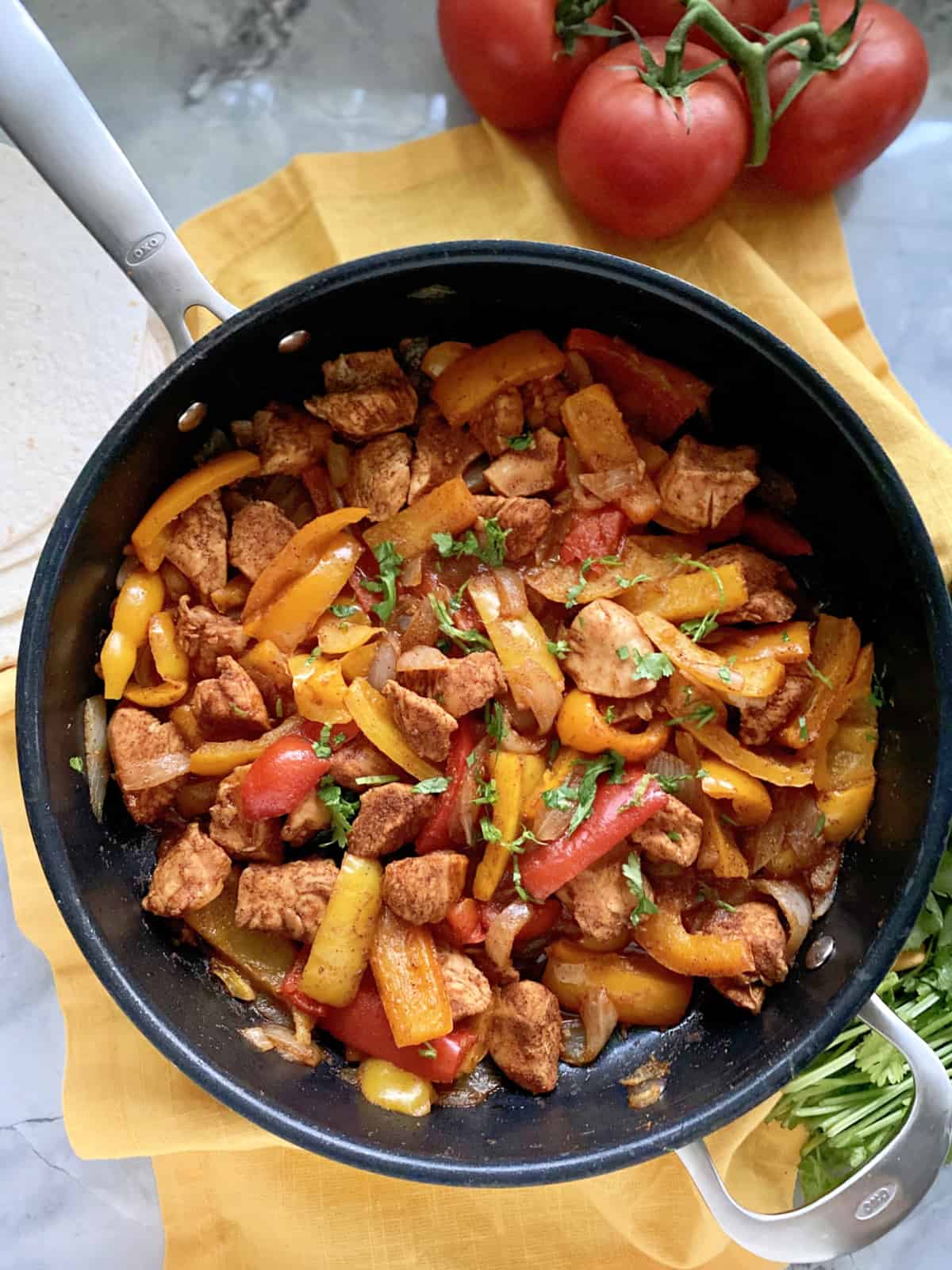 Top view of a skillet filled with chicken and bell peppers with tomatoes next to the skillet.