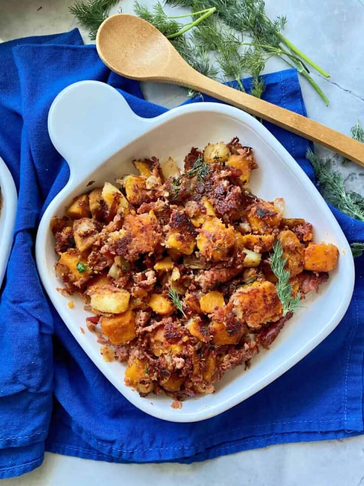 Top view of a white square plate full of Sweet Potato Corned Beef Hash on a colbalt blue cloth.