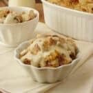 two white bowls filled with Apple Pie Bread Pudding with a casserole dish in the background.