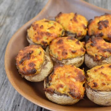 Brown baking dish filled with Buffalo Chicken Stuffed Mushrooms on a wood countertop.