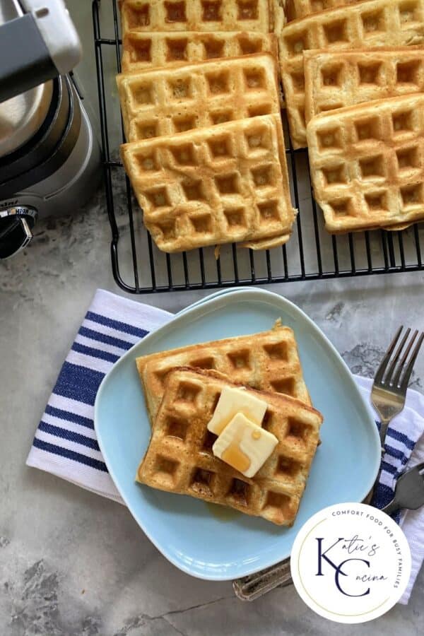 Top view of waffles on a blue plate with waffles on wire rack next to it with logo on right corner.