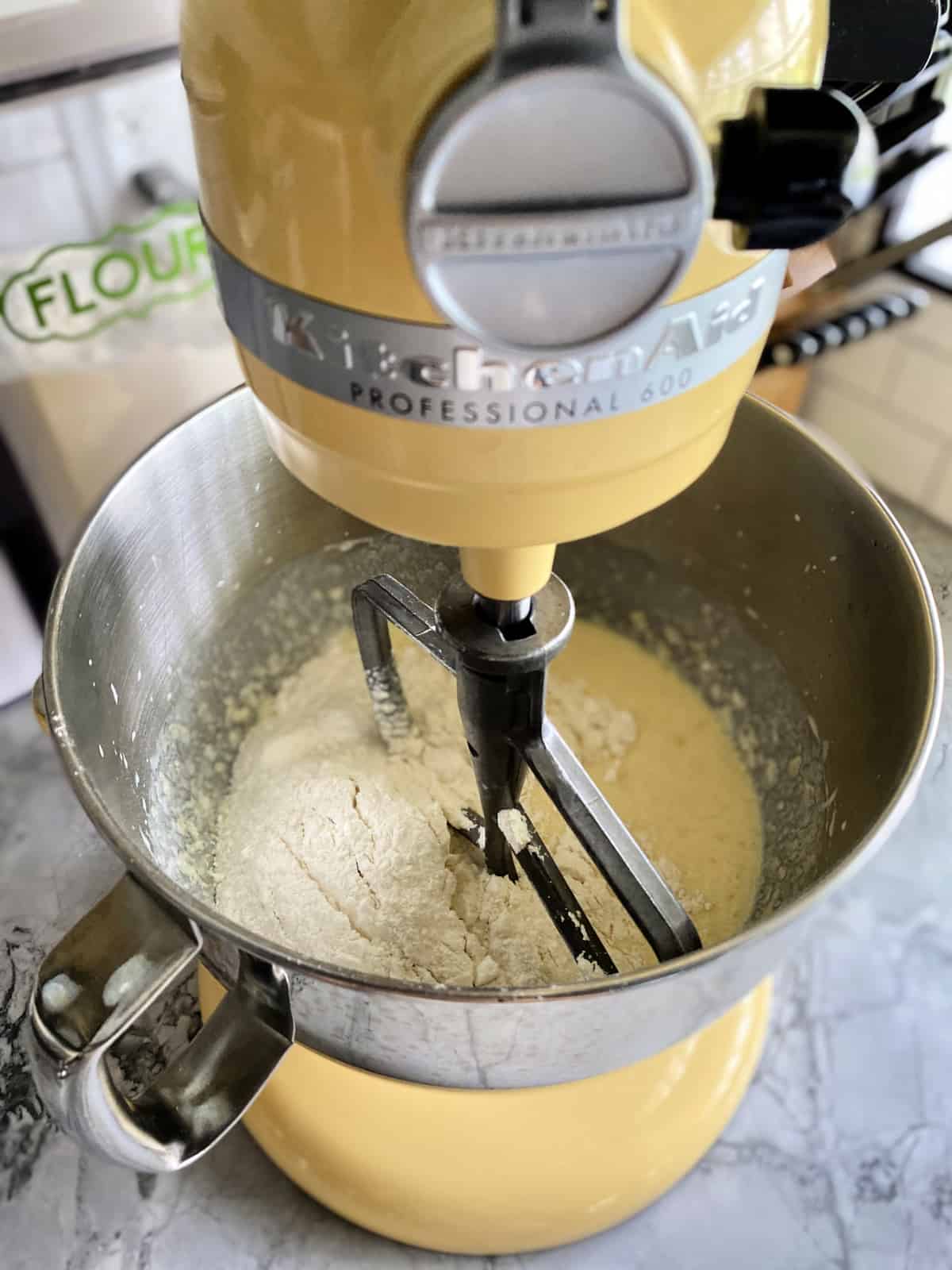 Yellow KitchenAid mixer with dry and wet ingredients in the bowl fitted with a paddle attachment.