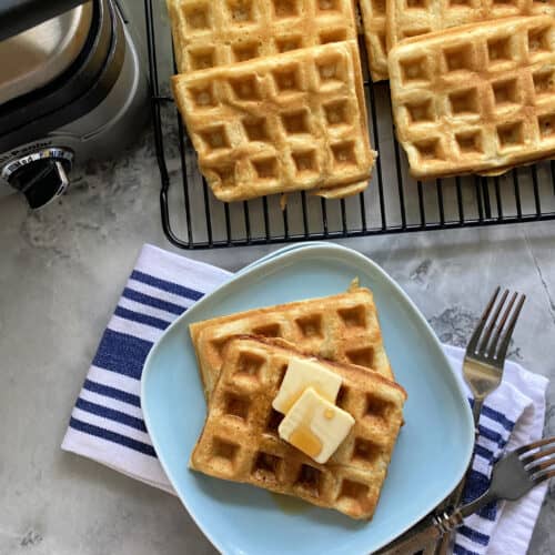 Top view of a blue plate filled with two waffles iwth butter and syrup with waffles and iron around it.