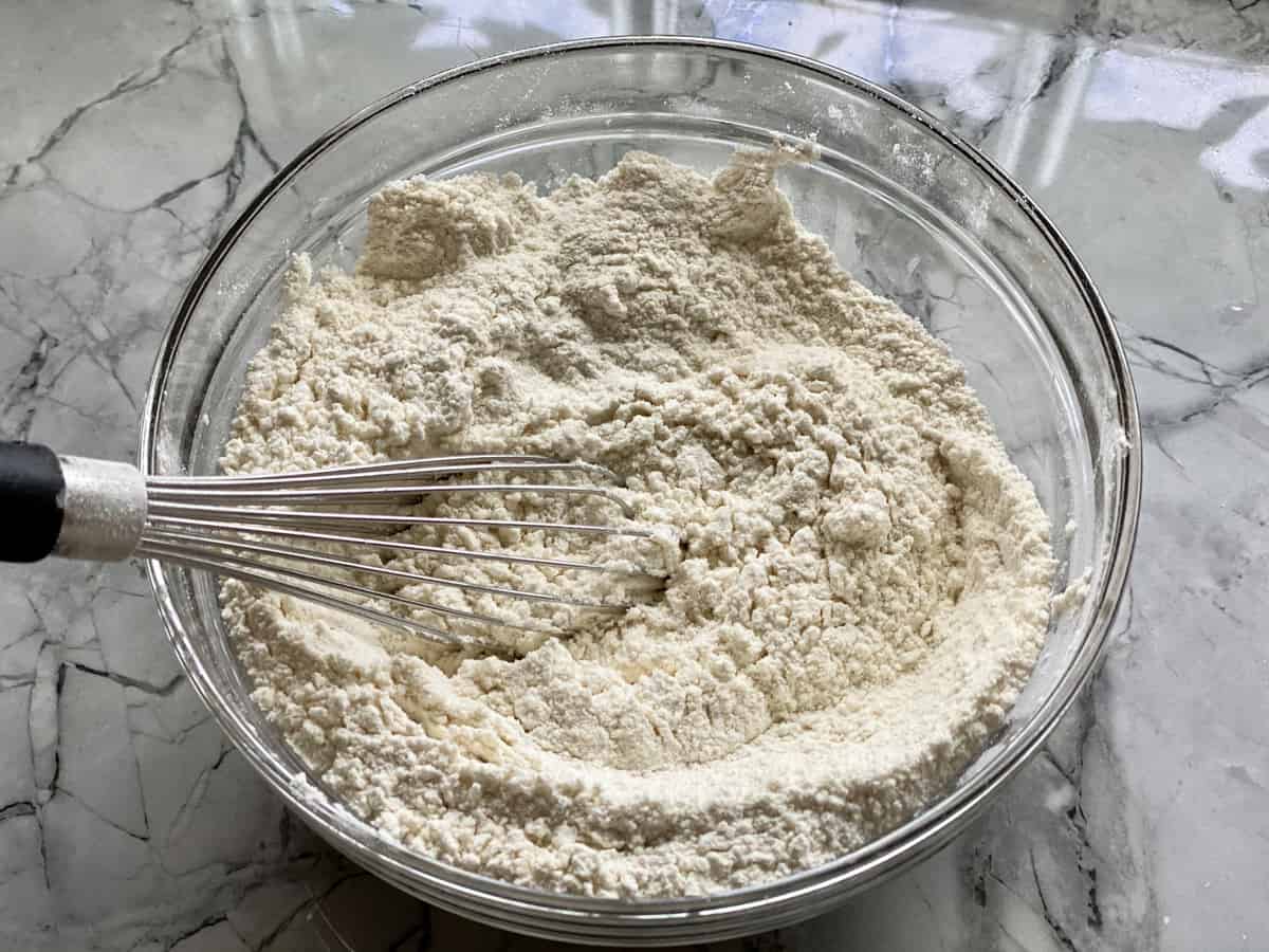 Top view of a glass bowl filled with flour and a whisk.