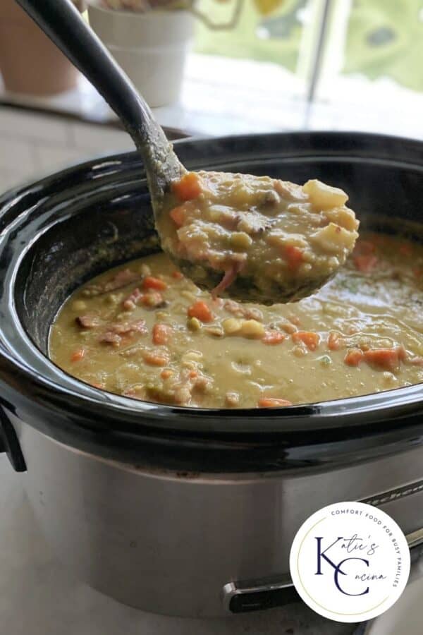 Black ladle holding split pea soup over a slow cooker with logo on bottom right corner.