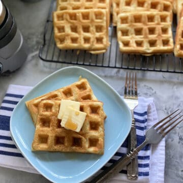 Top view of a blue plate with two waffles with wire rack full of waffles next to it.