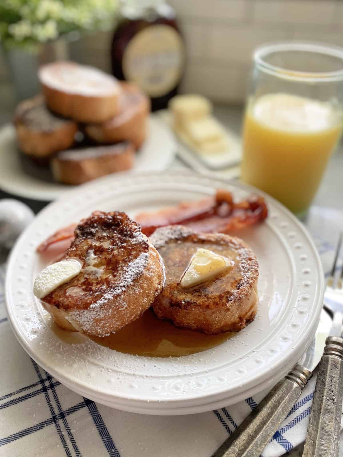 Two slices of french toast with bacon on a white plate with orange juice.