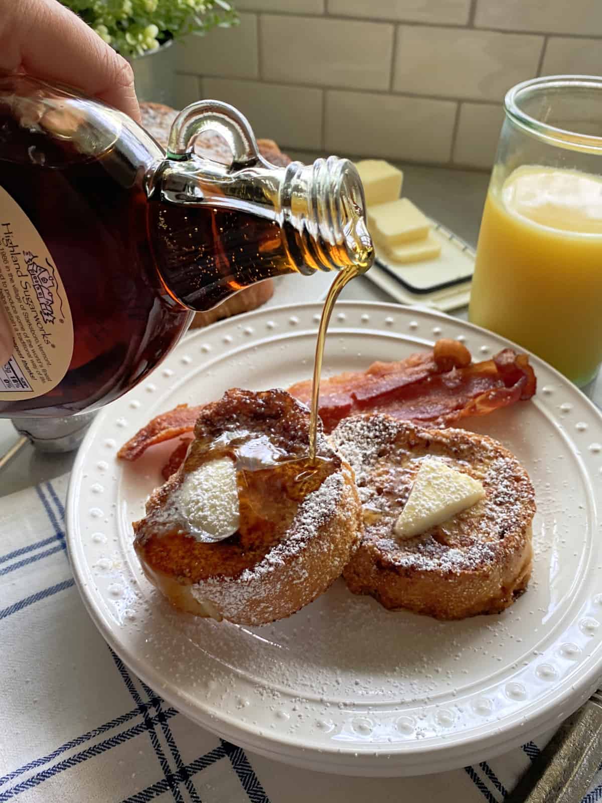 Hand pouring syrup over slices of french toast on a white plate.