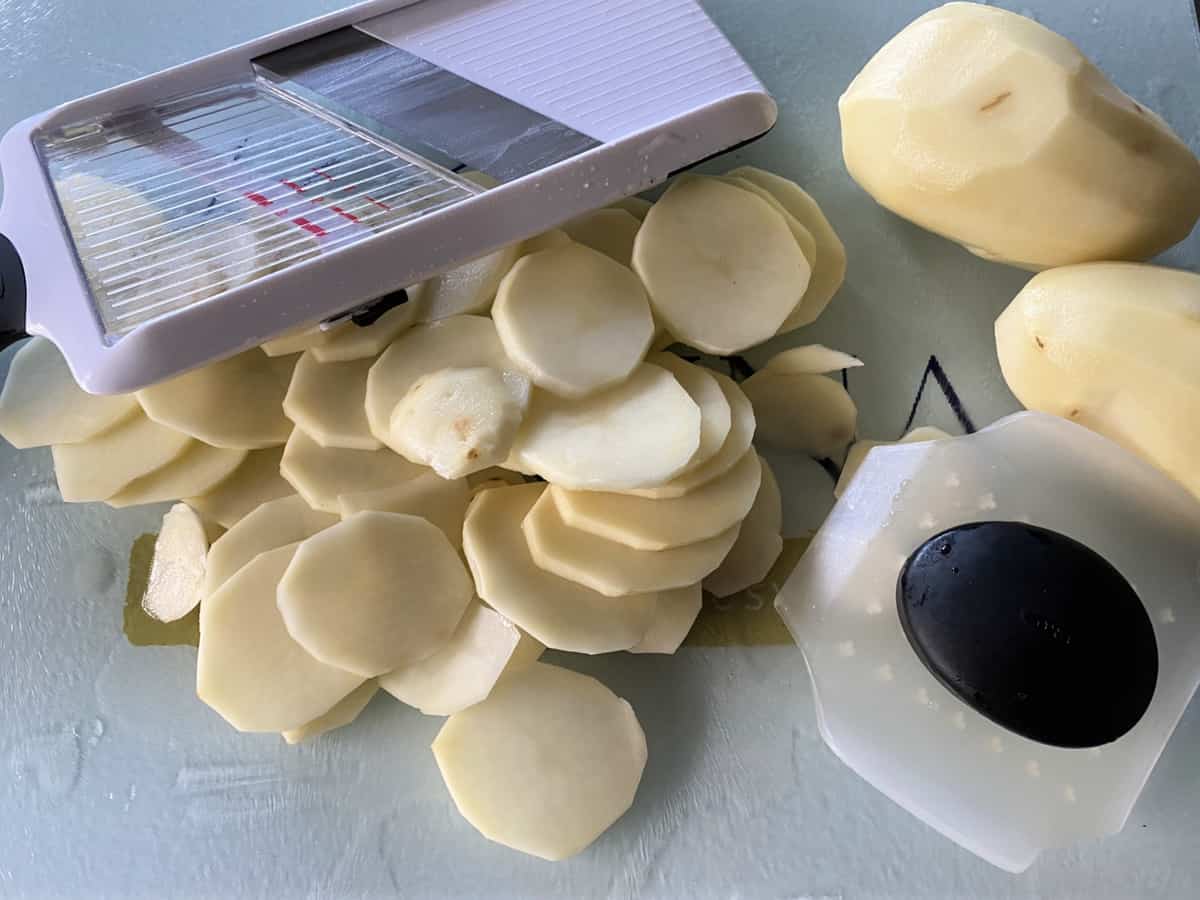 Hand held mandoline slicer with sliced potatoes next to it.