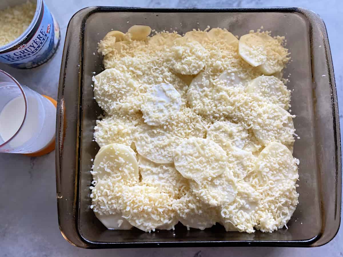 Top view of baking dish filled with raw sliced potatoes, cream, and cheese.