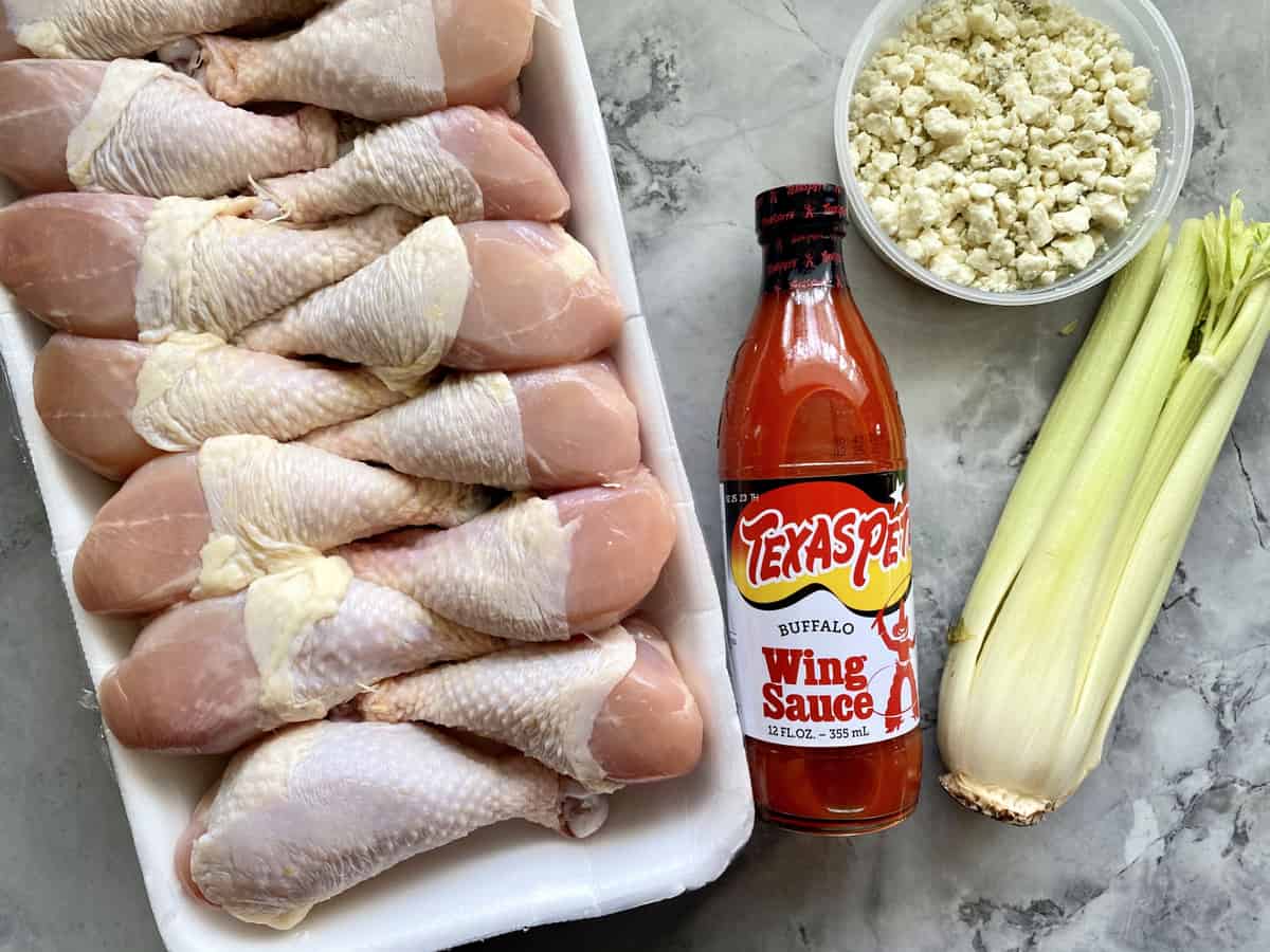 Ingredients on marble countertop: Chicken drumsticks, Texas Pete Buffalo Wing Sauce, Celery, and Bleu Cheese.