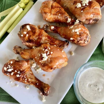 Top view of a white platter filled with Grilled Buffalo Chicken Drumsticks with bleu cheese.