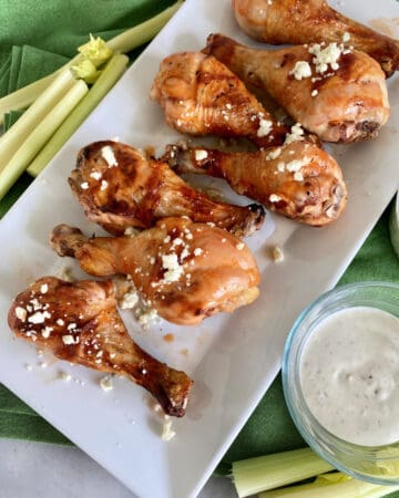 Top view of a white platter filled with Grilled Buffalo Chicken Drumsticks with bleu cheese.