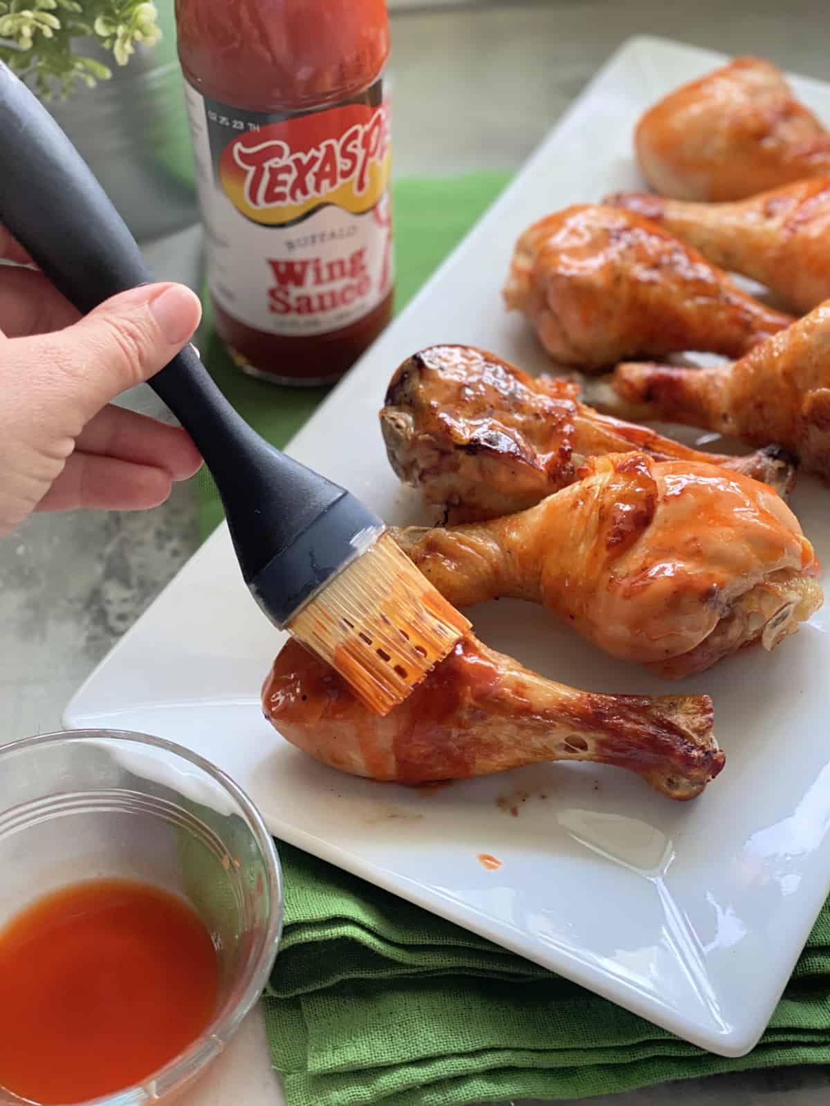 Female hand brushing on buffalo sauce on to chicken drumsticks.