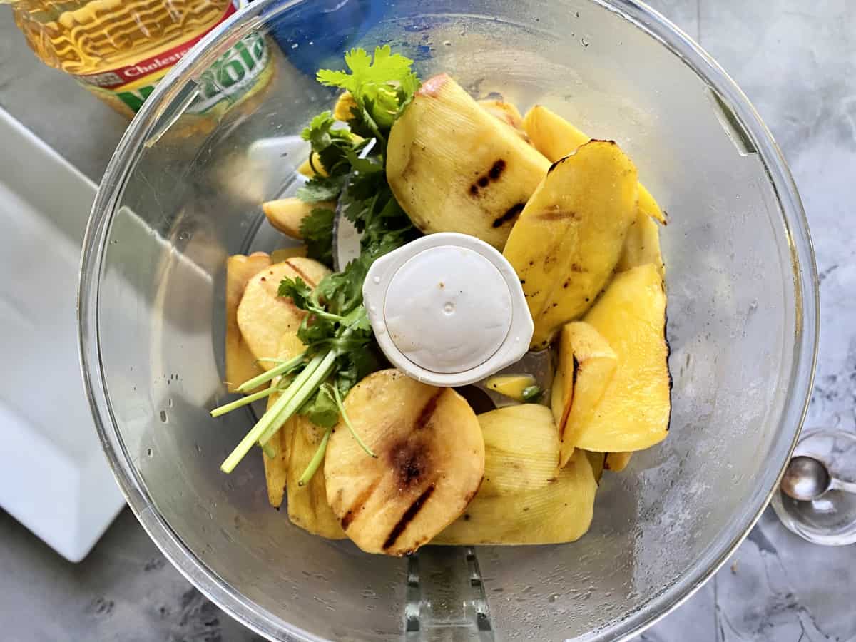 Top view of a food processor with grilled peaches and mangoes with cilantro.