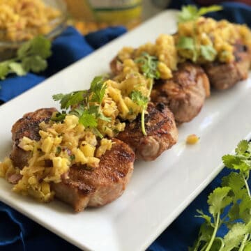 White platter with four pork chops topped with fruit salsa and cilantro on them.