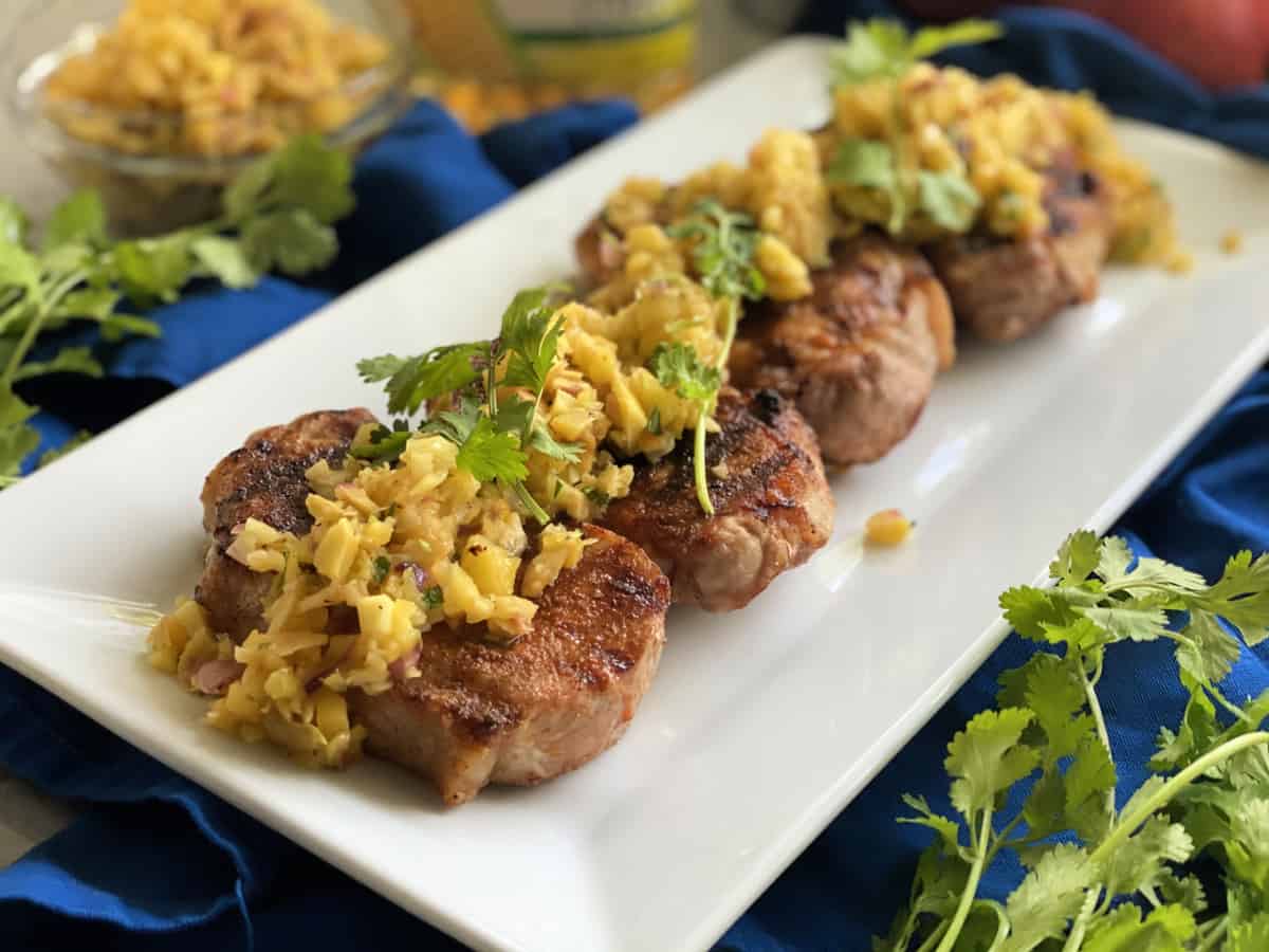 White platter with four pork chops topped with fruit salsa and cilantro on them.