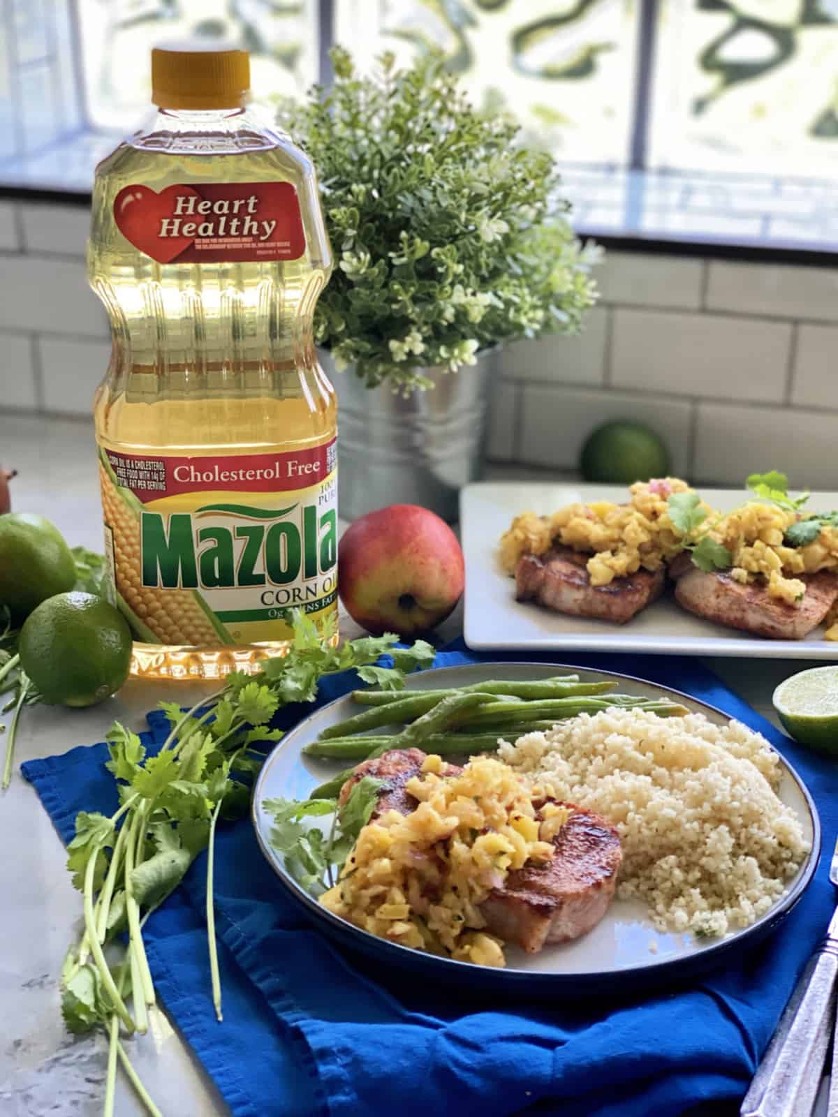 White plate filled with pork chops, fruit and couscous with a bottle of Mazola® Corn Oil in background.