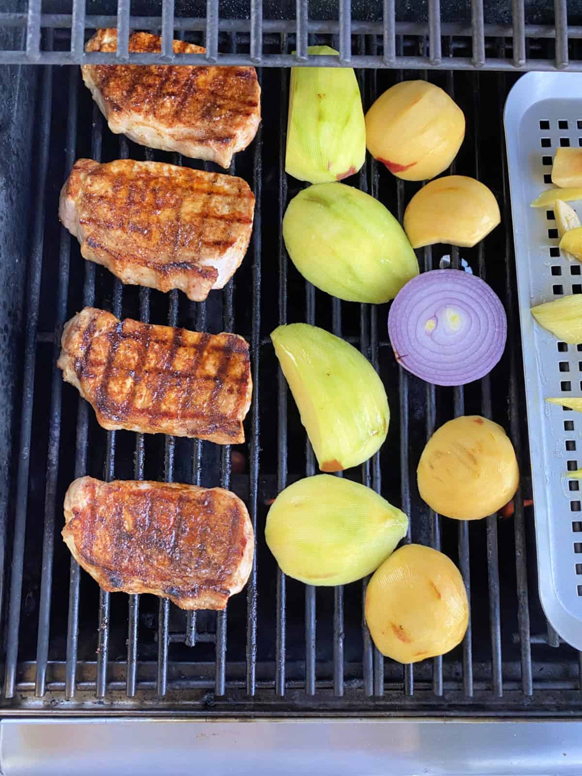 Top view of 4 grilled pork chops, sliced fruit and a red onion on a grill.