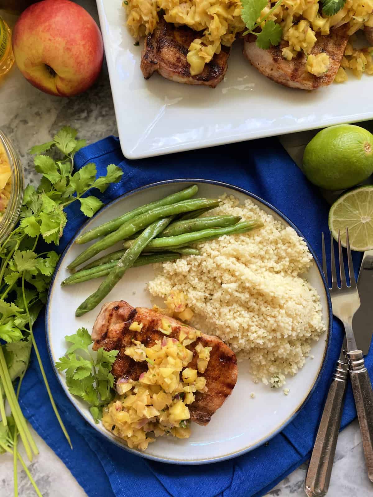 Top view of a plate and platter of pork chops, fruit salsa, couscous, and green beans.