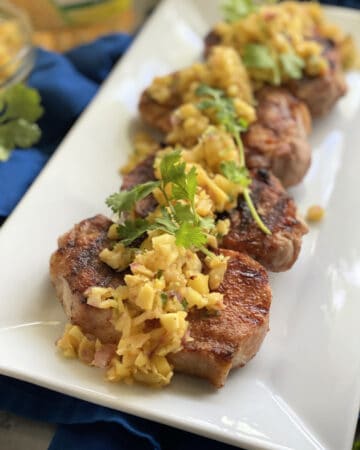 White platter filled with four grilled pork chops topped with fruit salsa and cilantro.