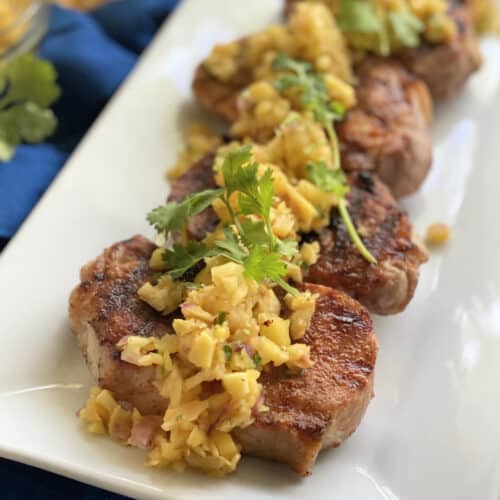 White platter filled with four grilled pork chops topped with fruit salsa and cilantro.