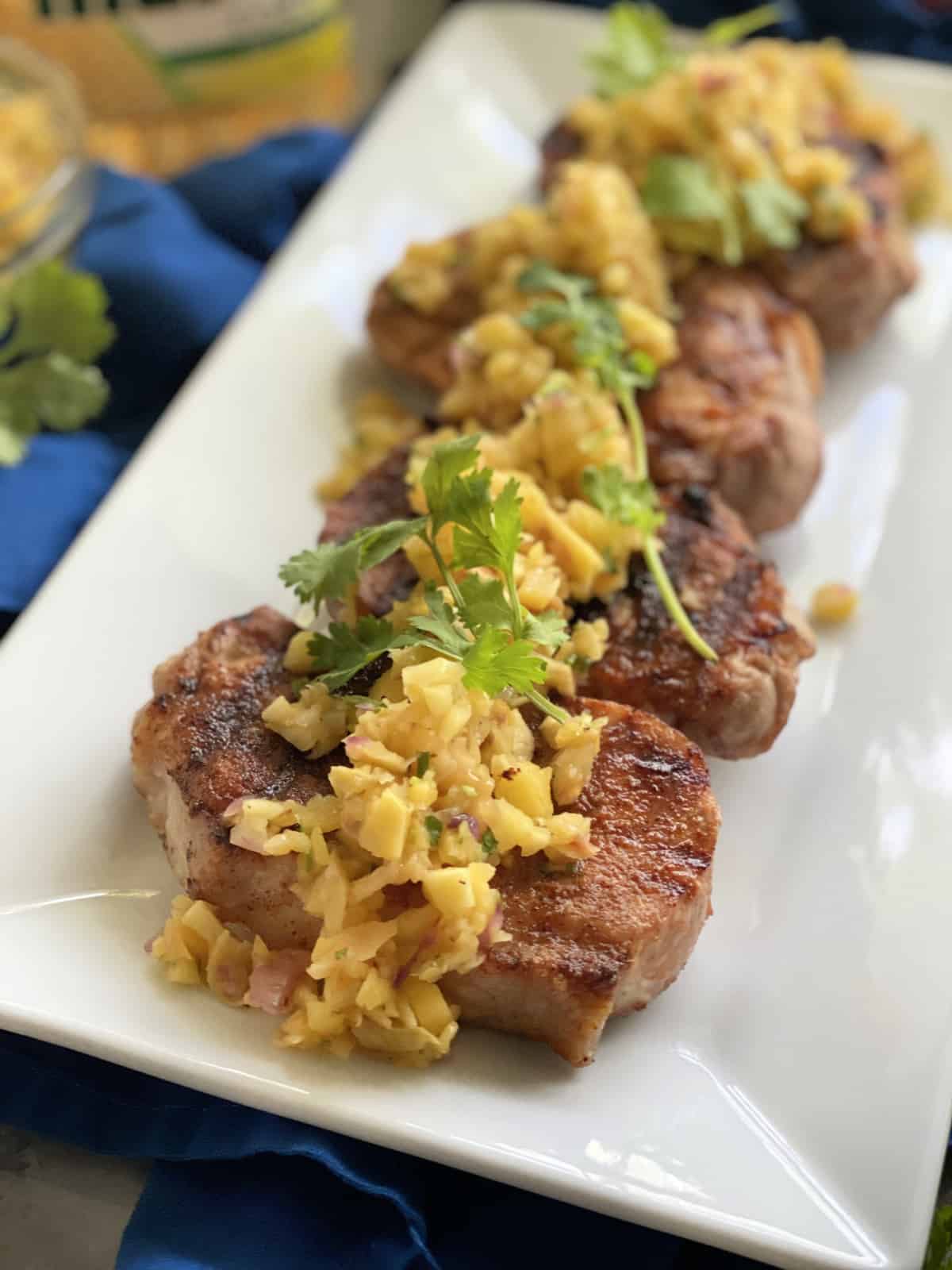 White platter filled with four grilled pork chops topped with fruit salsa and cilantro.