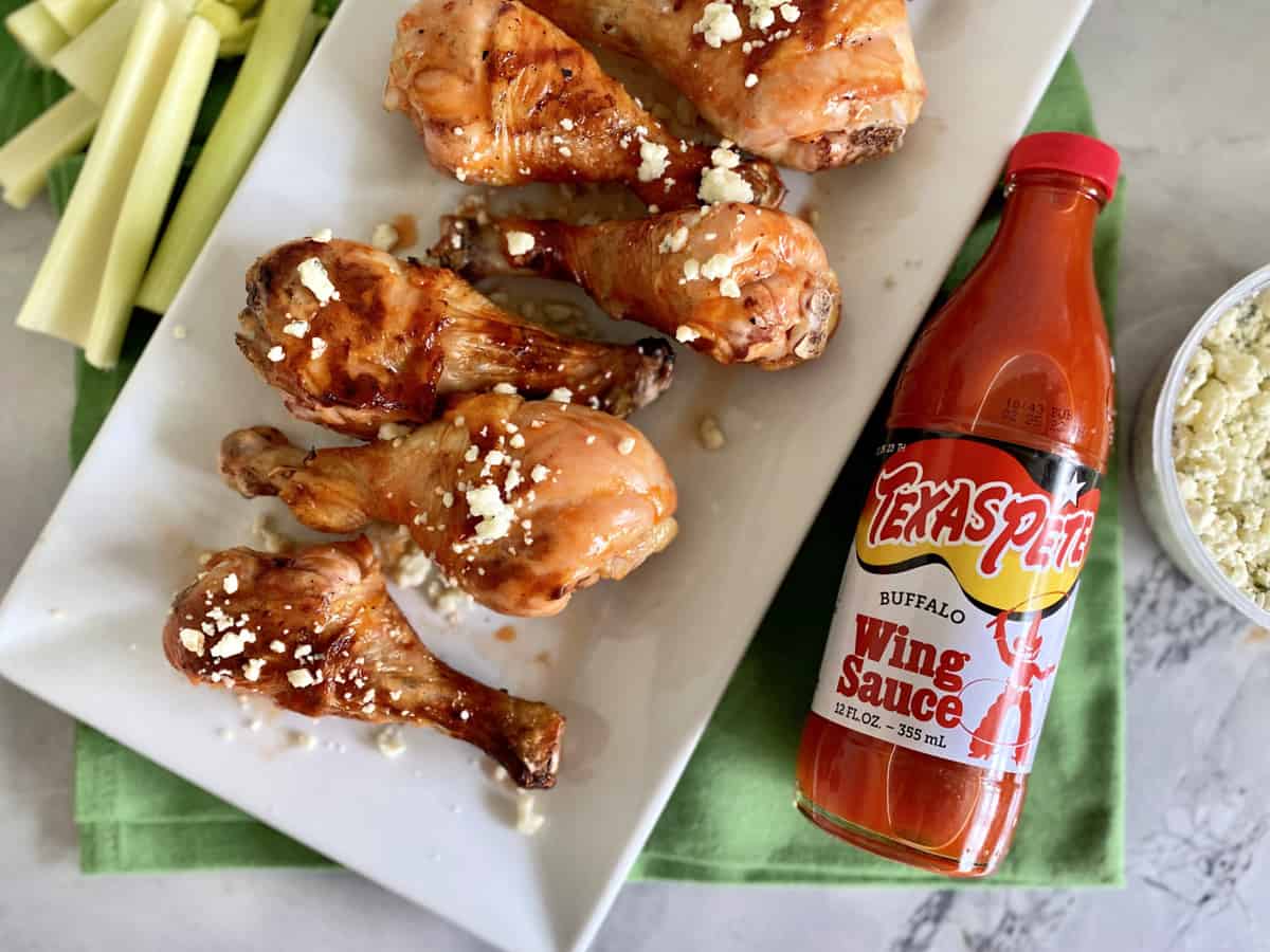 Top view of a white platter filled with Grilled Buffalo Chicken Drumsticks and Texas Pete Buffalo Wing Sauce bottle next to it.